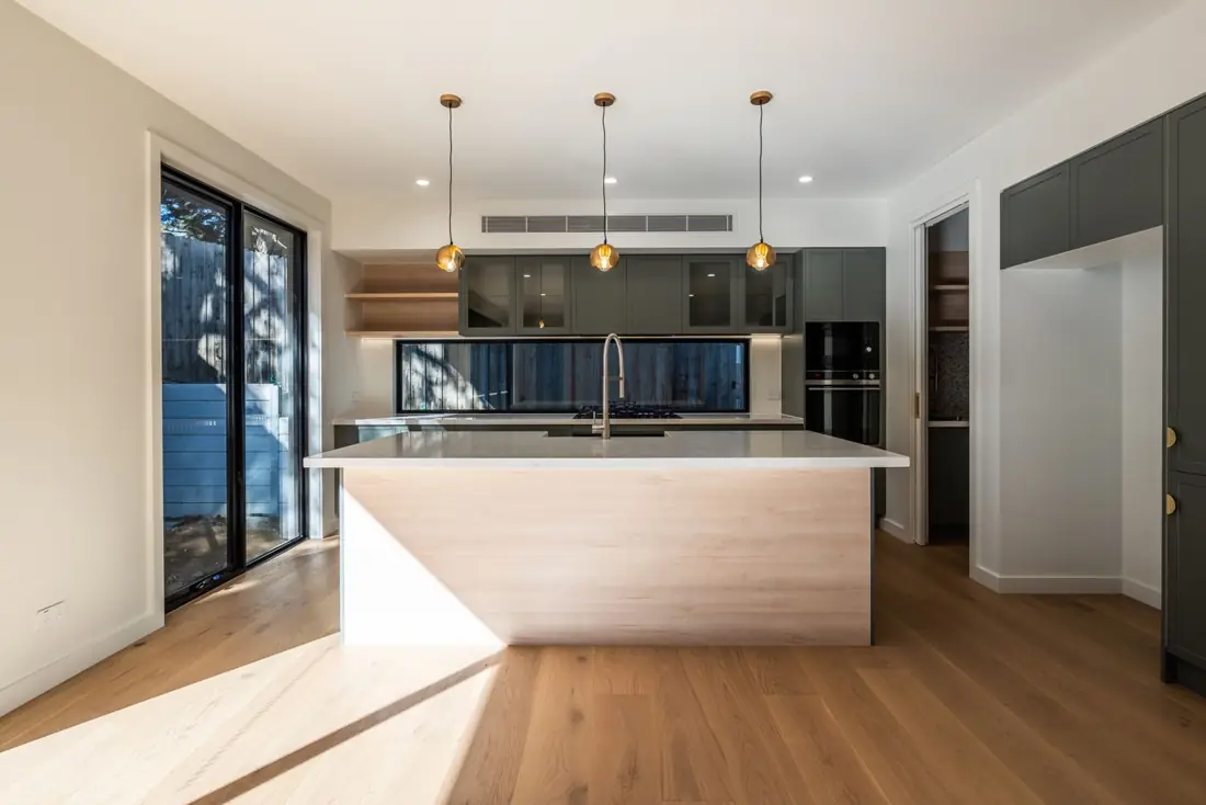 Finished kitchen with timber island bench, dark green cabinetry and brass pendant lights