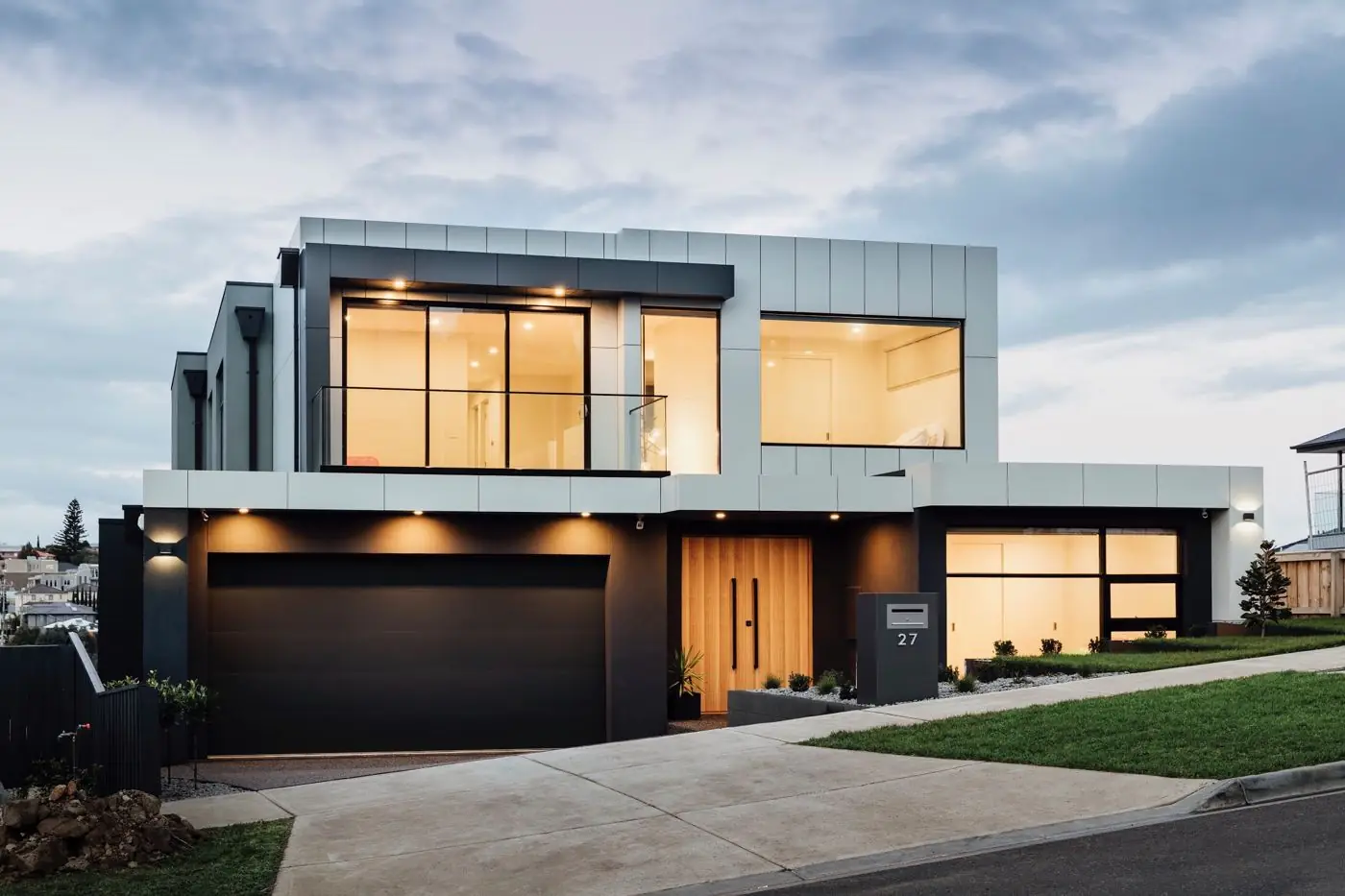 Modern double-storey home at dusk with lit windows and timber front door