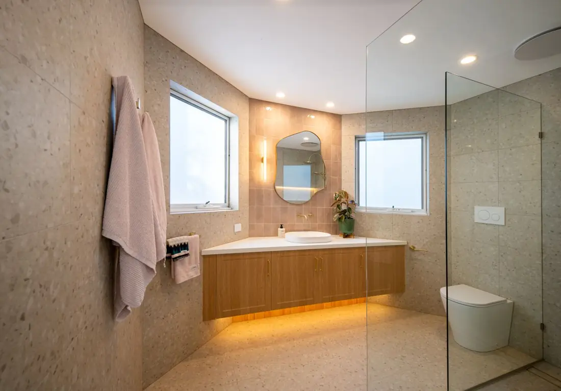 Bathroom with terrazzo tiles, floating timber vanity, pink feature tiles and brass fittings