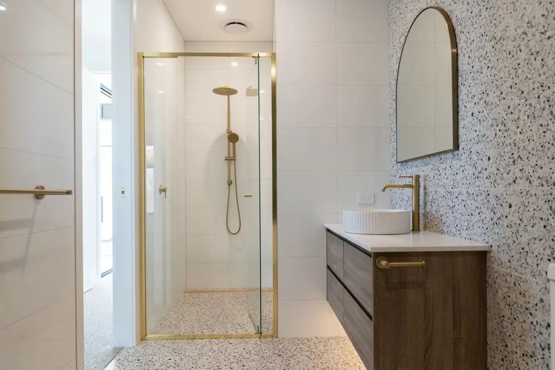 Bathroom with brass-framed shower screen, terrazzo tiles, arched mirror and timber vanity
