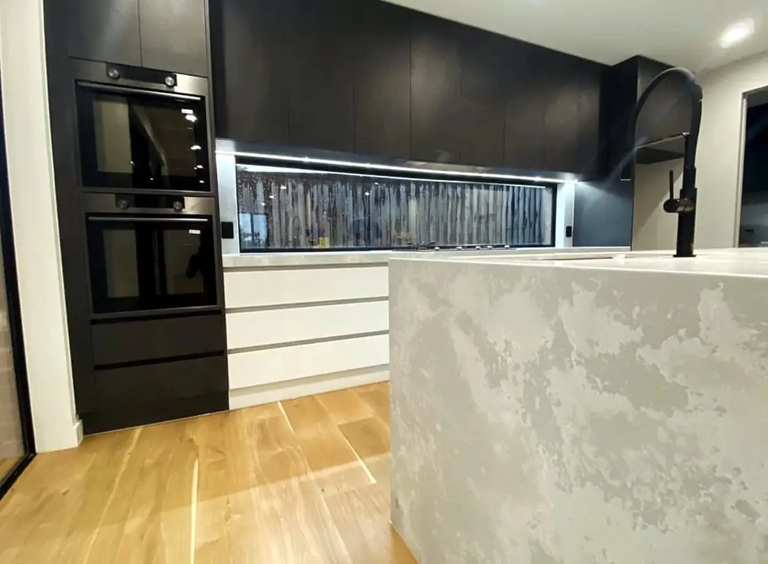 Kitchen with black cabinetry, stone waterfall island and window splashback